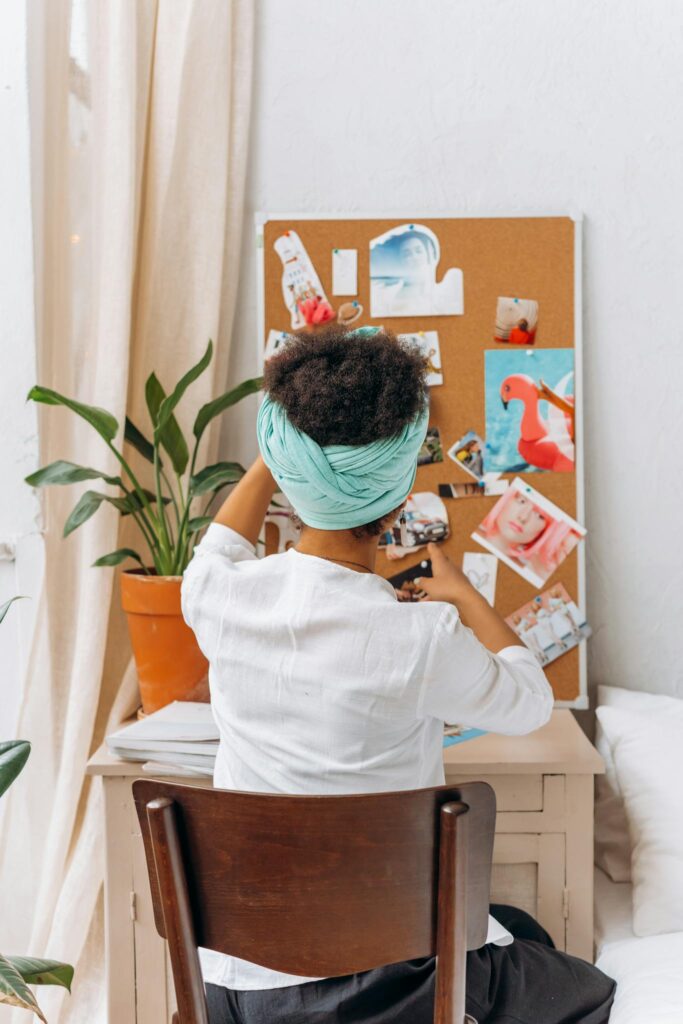 A woman sitting at a desk, engaging with her creative vision board at home, enhancing personal goals.