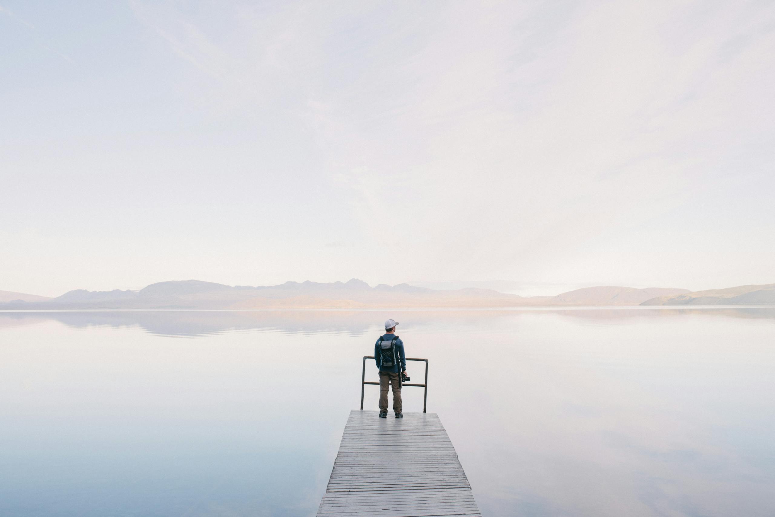 A solitary traveler stands on a dock enjoying the serene water view